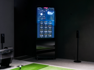A freestanding RangeX touchscreen kiosk displaying detailed golf swing metrics in an indoor simulator bay.